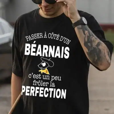 Homme portant un t-shirt noir à message béarnais humoristique « Passer à côté d’un Béarnais c’est un peu frôler la perfection », création locale Pilou Shop 64 à Pau
