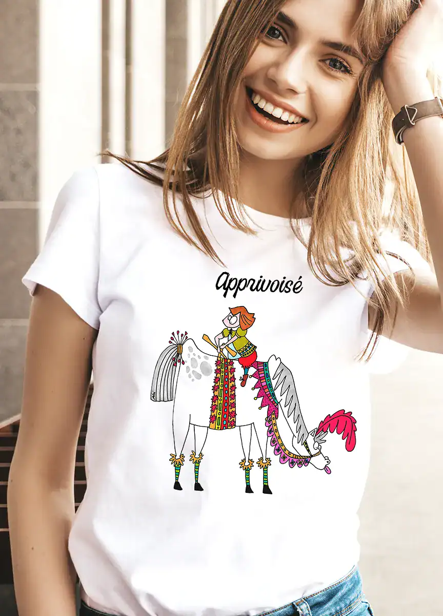 T-shirt femme blanc illustré « Apprivoisé » porté, illustration poétique Abi Illustration représentant une femme à cheval, style doux et coloré, vêtement féminin confortable et lumineux