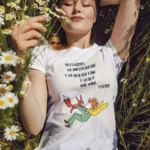 T-shirt femme blanc illustration Le Petit Prince et le renard avec citation poétique allongée dans un champ de marguerites vêtement littéraire artistique doux et intemporel
