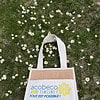 Sac sur herbe avec pâquerettes et logo AcoBeco