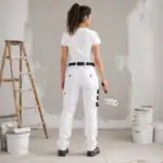 Femme peintre en bâtiment vue de dos portant un pantalon ilkott de travail blanc dans une ambiance chantier rénovation BTP avec rouleau de peinture.