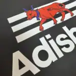 Gros plan du marquage DTF sur un t-shirt noir Adishatz Béarn, avec vache rouge, bandes blanches et lettrage blanc.