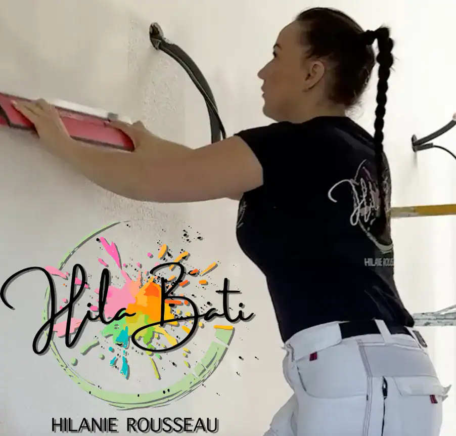 Hilanie Rousseau de Hila Bâti en tenue de peintre bâtiment réalisant des travaux de finition murale avec règle de lissage intérieure