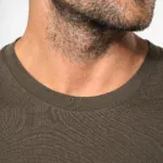 Détail du col rond d’un t-shirt homme manches longues kaki porté par un homme barbu.
